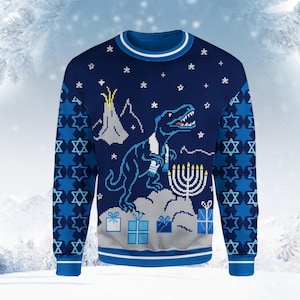 May include: A dark blue long-sleeve jumper featuring a pixelated graphic of a dinosaur wearing a scarf, standing next to a menorah and a volcano. The design includes white snowflakes, gift boxes, and a repeating pattern of Stars of David.