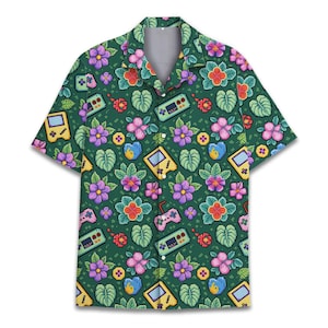 May include: Short-sleeved button-down shirt with a green background and a pattern of pixelated video game controllers, handheld consoles, and tropical flowers in pink, purple, and red. The shirt has a classic collar.