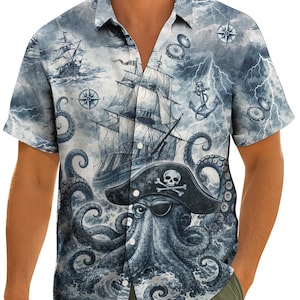 Puede incluir: Camisa de manga corta con diseño de temática pirata. La camisa presenta una ilustración detallada de un barco pirata, un pulpo, brújulas y rayos en tonos azules y grises.