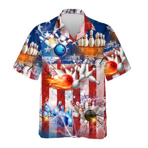May include: Short-sleeved button-down shirt with a bowling theme. The shirt features a graphic design of bowling pins, bowling balls, and lightning bolts against a backdrop of red and white stripes and blue stars.