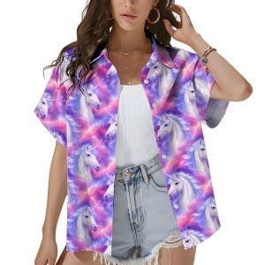 Könnte beinhalten: Kurzärmeliges Button-Down-Hemd mit einem sich wiederholenden Muster aus weißen Einhörnern mit blauen Mähnen und Hörnern vor einem Hintergrund aus rosa und lila Wolken. Das Hemd hat einen klassischen Kragen und ist aus leichtem Stoff gefertigt.