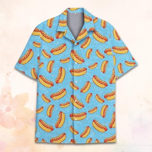 May include: A short-sleeved button-down shirt with a light blue background and a repeating pattern of cartoon hot dogs. The hot dogs are yellow with red accents, and the shirt has a classic collar.