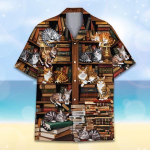 May include: A brown and white short-sleeved button-up shirt featuring a pattern of cats on bookshelves. The cats are in various poses, some sleeping, some sitting, and some standing. The bookshelves are filled with books of different sizes and colours.