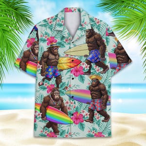 Op de afbeelding: Lichtblauw overhemd met knopen met een herhaald patroon van cartoon Bigfoot-personages met surfplanken, zonnebrillen en bloemaccenten. Het shirt heeft een klassieke kraag en korte mouwen.