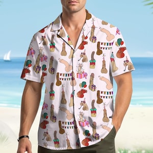 May include: White short-sleeve button-down shirt with a repeating pattern of cartoon penises decorated with party hats, candles, and balloons. The shirt has a classic collar and is worn by a person standing in front of a beach scene.