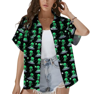 May include: Black button-up shirt with a repeating pattern of green aliens and UFOs. The aliens have large black eyes and are standing on gray flying saucers. The shirt is short-sleeved and has a collared neckline.