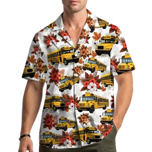May include: Short-sleeved button-down shirt with a white background and a repeating pattern of yellow school buses, red and orange flowers, and green leaves. The shirt has a classic collar and a relaxed fit.