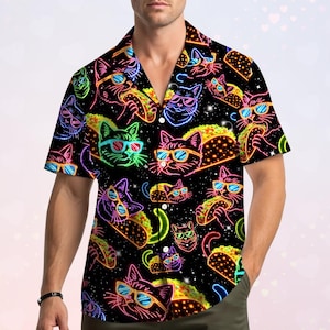 May include: A short-sleeved button-down shirt with a black background featuring a repeating neon-colored pattern of cats wearing sunglasses and eating tacos. The design includes vibrant outlines in pink, blue, green, and yellow against a dark field.
