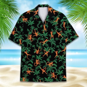 Pode incluir: Camisa preta de manga curta com um padrão tropical de macacos laranja e folhas verdes. A camisa tem uma gola clássica e um corte descontraído. O design é apresentado sobre um fundo preto, ideal para o verão.