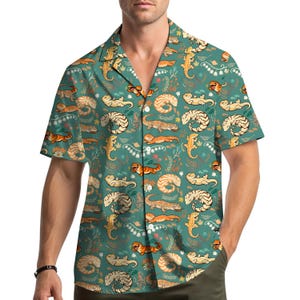 May include: Short-sleeved button-down shirt with a teal background and a repeating pattern of lizards in various poses and colors. The lizards are tan, orange, and cream, with floral and leaf accents. The shirt has a classic collar and a relaxed fit.