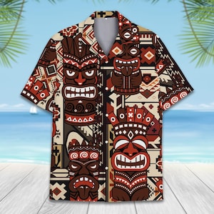 Puede incluir: Una camisa de manga corta con botones que presenta un patrón repetitivo de máscaras tiki marrones y rojo oscuro sobre un fondo crema. El diseño incluye formas geométricas y motivos de inspiración tribal integrados en el estampado.