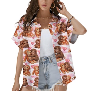 Può includere: Camicia a maniche corte con un motivo ripetuto di scimmie dei cartoni animati e cuori rosa su sfondo bianco. Le scimmie sono in varie pose, alcune si abbracciano. La camicia ha una vestibilità ampia.