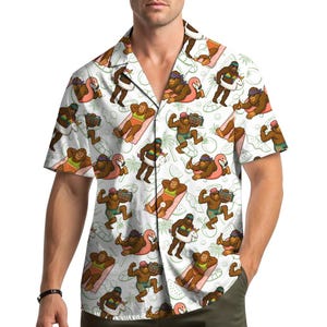 Könnte beinhalten: Weißes Button-Down-Hemd mit einem sich wiederholenden Muster eines Cartoon-Bigfoot, der Sommeraktivitäten genießt. Bigfoot wird mit Sonnenbrille, Badehose und Accessoires wie einer Boombox und einem aufblasbaren Flamingo dargestellt. Das Hemd hat kurze Ärmel und eine lockere Passform.