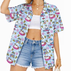 May include: A light blue short-sleeve button-down shirt featuring an all-over print of white ducks in pink inner tubes, wearing sunglasses and hats, with the text "it's summer time" scattered throughout the pattern, paired with blue denim shorts.