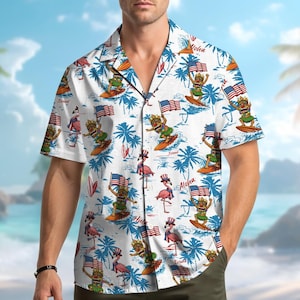 May include: White short-sleeve button-down shirt with a tropical print. The design features cartoon figures surfing with American flags, palm trees, and flamingos. The word "Aloha" is printed on the shirt.