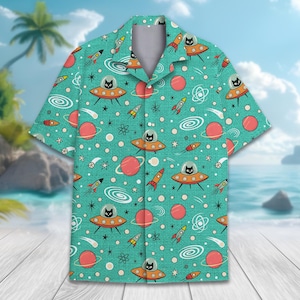 May include: A short-sleeved button-down shirt in teal featuring an all-over space print. The pattern includes black cats inside orange flying saucers, red planets with rings, colorful rockets, white spiral galaxies, and small stars.