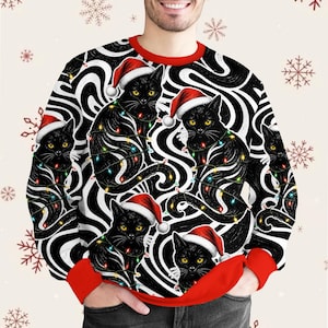 Peut inclure: Un sweat-shirt à col rond et manches longues arborant un motif répétitif de chats noirs portant des bonnets de Noël rouges et entourés de guirlandes lumineuses colorées sur un fond hypnotique noir et blanc avec des poignets et un col rouges.
