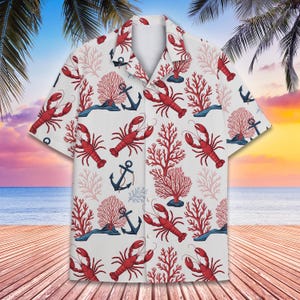 以下が含まれることがあります： 赤いロブスター、サンゴ、錨が描かれたトロピカル柄の白いボタンダウンシャツ。シャツは半袖で、クラシックな襟です。