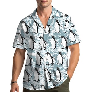May include: Short-sleeved shirt with a repeating pattern of black and white penguins on a light blue, distressed background. The shirt has a classic collar and a relaxed fit, suitable for casual wear.