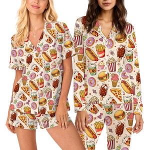 May include: Cream-coloured pyjama set featuring a repeating pattern of fast food items. The pattern includes pizza slices, burgers, ice cream, donuts, and coffee cups. The set includes a short-sleeved top and shorts.