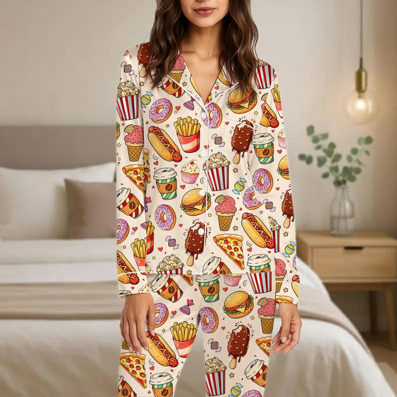 May include: Cream-coloured two-piece pyjama set with a repeating pattern of fast food items, including burgers, pizza, ice cream, and donuts. The pyjamas have white trim and a button-down top.
