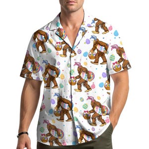 May include: White button-down shirt with a repeating pattern of a brown Bigfoot character wearing bunny ears and carrying a basket of Easter eggs. The shirt also features colorful Easter eggs and polka dots.