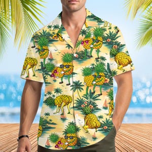 Puede incluir: Una camisa de manga corta con botones y un estampado de playa tropical con palmeras, veleros y piñas de dibujos animados. Las piñas tienen brazos, piernas y gafas de sol, y aparecen realizando diversas actividades sobre un fondo amarillo.