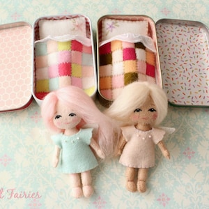 Puede incluir: Dos muñecas de fieltro con pelo rosa y rubio están tumbadas en camas en miniatura hechas de latas reutilizadas. Las camas tienen edredones de patchwork coloridos y las muñecas llevan vestidos sencillos.