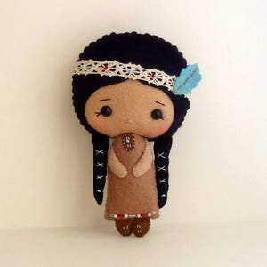 May include: A felt doll with black hair, brown eyes, and a brown dress. The doll is wearing a white lace headband and a blue feather.
