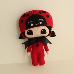 May include: A red felt ladybug doll with black spots and a black bow. The doll has a black felt face with white cheeks and black eyes.