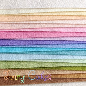May include: A stack of felt fabric in various colors, including white, cream, peach, pink, purple, blue, green, brown, and beige. The felt is arranged in a rainbow pattern. The text "Fairy Cakes" is visible at the bottom of the image.