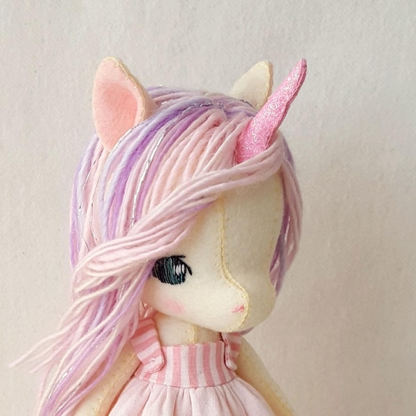 May include: A handmade felt unicorn doll with pink and purple yarn hair, a pink glitter horn, a pink and white striped dress, and white shoes.
