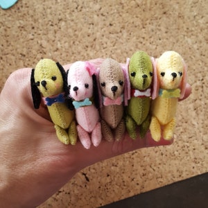 Puede incluir: Cinco pequeños peluches de perro de fieltro en diferentes colores, incluyendo verde, rosa, marrón, amarillo y verde claro. Cada peluche tiene una corbata de lazo de color diferente y una nariz negra.