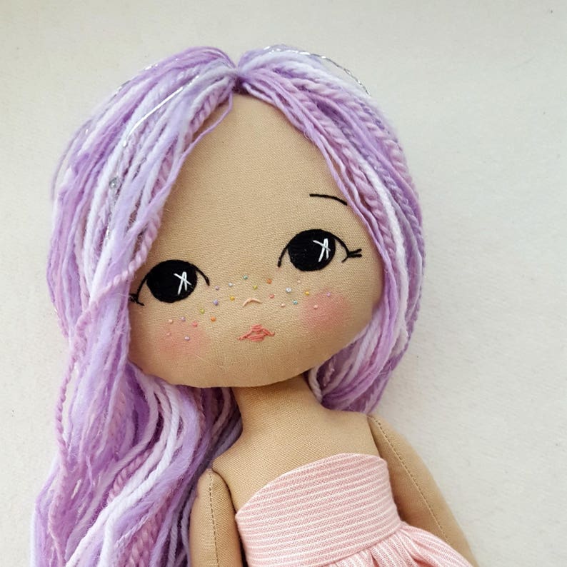 May include: A handmade doll with long, wavy purple and white hair. The doll has a pink and white striped dress and embroidered facial features.