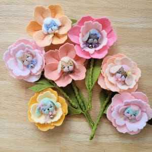 Peut inclure: Un bouquet de fleurs en feutre faites à la main, aux couleurs pastel variées, chacune avec un petit visage de chiot fantaisiste au centre. Les fleurs ont des tiges et des feuilles en feutre vert, créant un charmant bouquet artisanal.