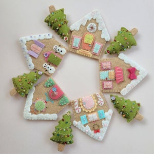 May include: Nine felt ornaments in the shape of gingerbread houses and Christmas trees. The houses are decorated with colorful details, including candy canes, windows, and doors. The trees are green with white and gold embellishments.