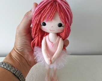 May include: A handmade doll with a pink dress and a white tutu. The doll has red yarn hair and rosy cheeks. The doll is wearing pink ballet shoes. The doll is approximately 6 inches tall.