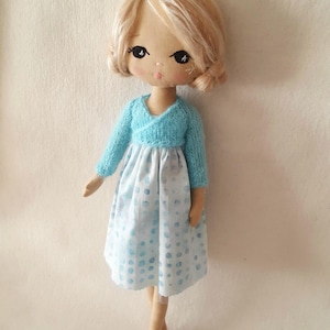 May include: A handmade doll with blonde hair, wearing a light blue sweater and a white dress with blue polka dots.
