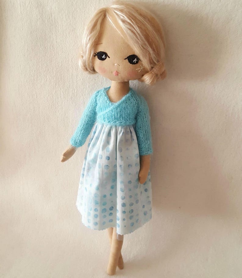 May include: A handmade doll with blonde hair, wearing a light blue sweater and a white dress with blue polka dots.