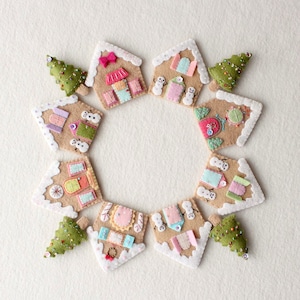 May include: A circle of felt gingerbread houses with white frosting and colorful details, decorated with felt snowmen and Christmas trees.
