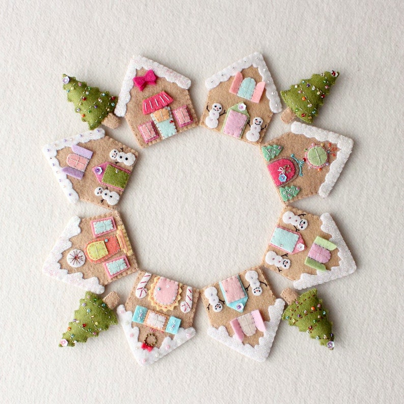 May include: A circle of felt gingerbread houses with white frosting and colorful details, decorated with felt snowmen and Christmas trees.