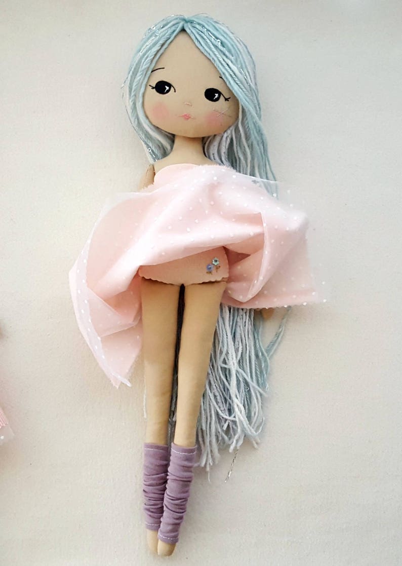 May include: A handmade doll with long, light blue yarn hair, wearing a pink tulle skirt with white polka dots and purple leg warmers.
