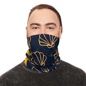Könnte beinhalten: Ein marineblaues Halstuch mit einem sich wiederholenden goldenen Muschelmuster. Das Halstuch wird um den Hals getragen und bedeckt das untere Gesicht. Der Hintergrund ist weiß.