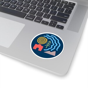 May include: A round sticker featuring a colorful abstract design. The design includes a yellow spiral, a red arch, a green tree, blue wavy lines, and a pink and gray mountain shape, all set against a dark blue background.
