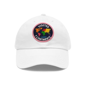May include: White baseball cap with a circular patch showing a colourful world map. The patch reads "VISITED 7 CONTINENTS" in dark blue, with a pink border. The cap has a curved peak and a classic, adjustable design.