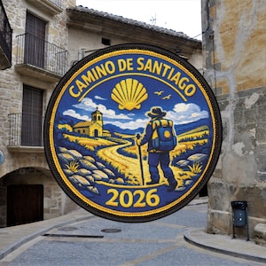 Pode incluir: Remendo circular com as palavras "Camino de Santiago" em letras douradas sobre fundo azul. O remendo apresenta um peregrino caminhando por um caminho, uma igreja e o ano de 2026. Uma concha amarela na parte superior.
