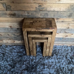 May include: Three wooden nesting tables with a rustic finish. The tables are stacked on top of each other and are sitting on a grey shag rug.