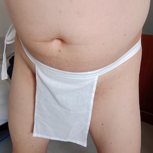 Op de afbeelding: Een witte fundoshi, een traditioneel Japans ondergoed, wordt getoond. De fundoshi is gemaakt van witte stof en heeft een rechthoekig paneel aan de voorkant. Het kledingstuk wordt met een wit touwtje om de taille geknoopt.