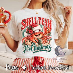 Puede incluir: Una camiseta blanca con el gráfico de un cangrejo sonriente con gorro de Papá Noel, rodeado de ramas de pino, una estrella de mar y un adorno a rayas. El texto dice "SHELL YEAH It's Christmas" en letras rojas y verdes.