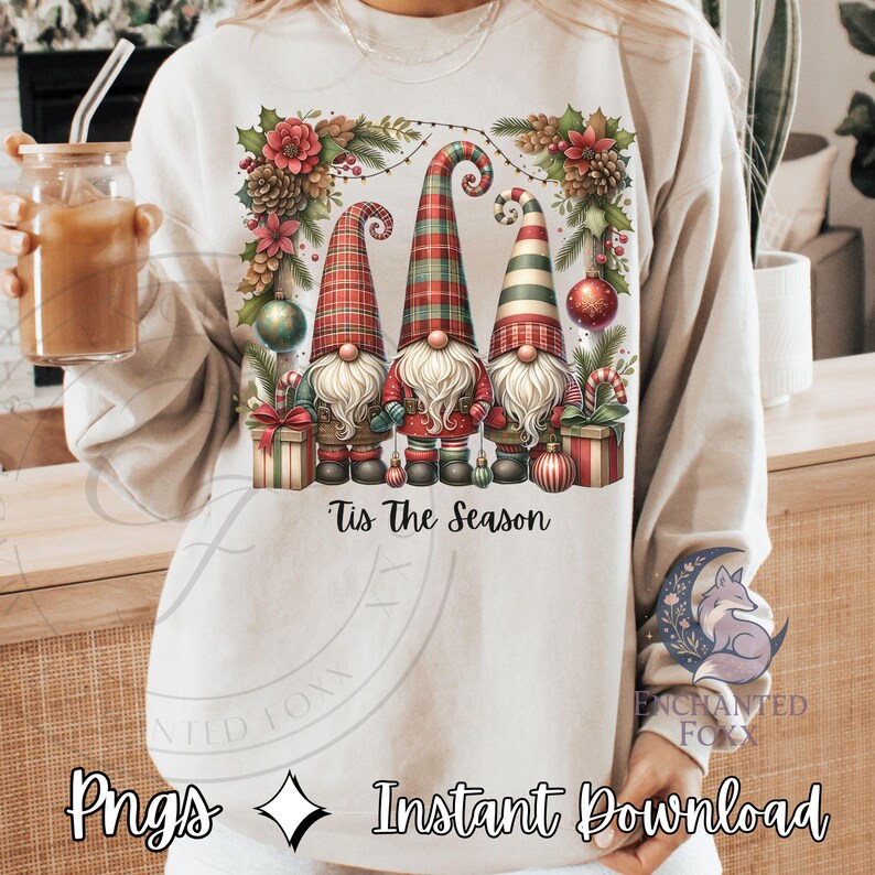 A person wearing a white sweater with a graphic design of three gnomes surrounded by Christmas decorations, including ornaments, pine cones, and a wreath. The person is holding a drink in their hand.